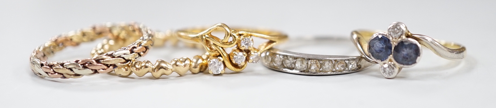 Three assorted white or yellow metal and gem set rings, including sapphire and diamond four stone cross over ring and a graduated diamond chip set half eternity ring, a similar three colour band, gross weight 8 grams and